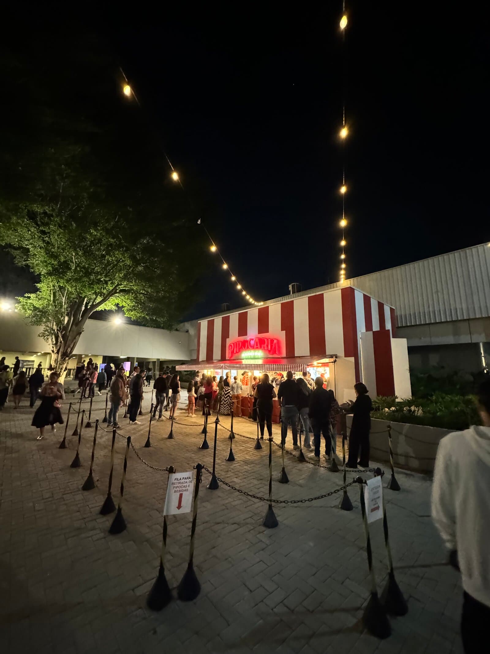 Multidão organizada em fila na fachada Pipocaria Premium à noite