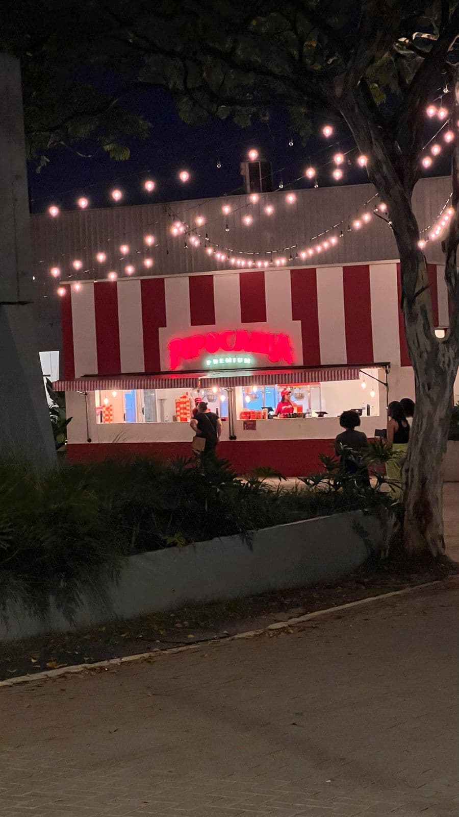 Fachada Pipocaria Premium iluminada à noite com luzes de varal